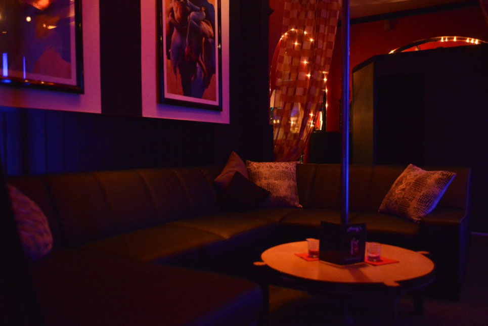 Dunkle Sitzecke mit Ecksofa, rundem Tisch und einer Stange.